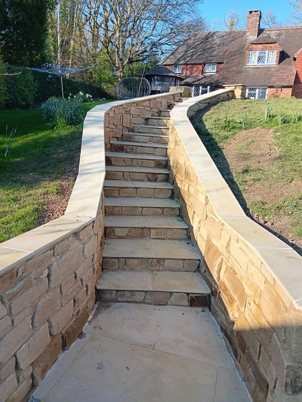 Sweeping curved sandstone staircase rising between natural stone retaining walls